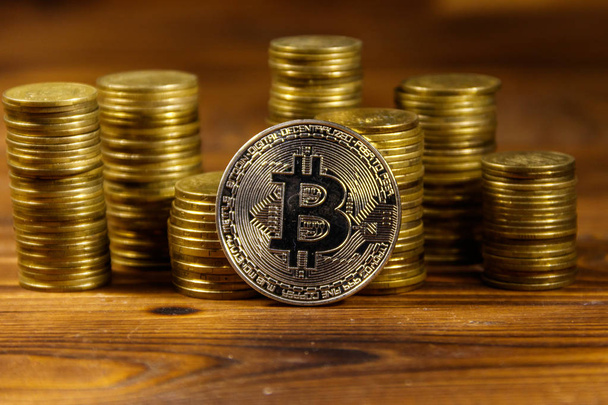 Silver bitcoin and stacks of coins on wooden background